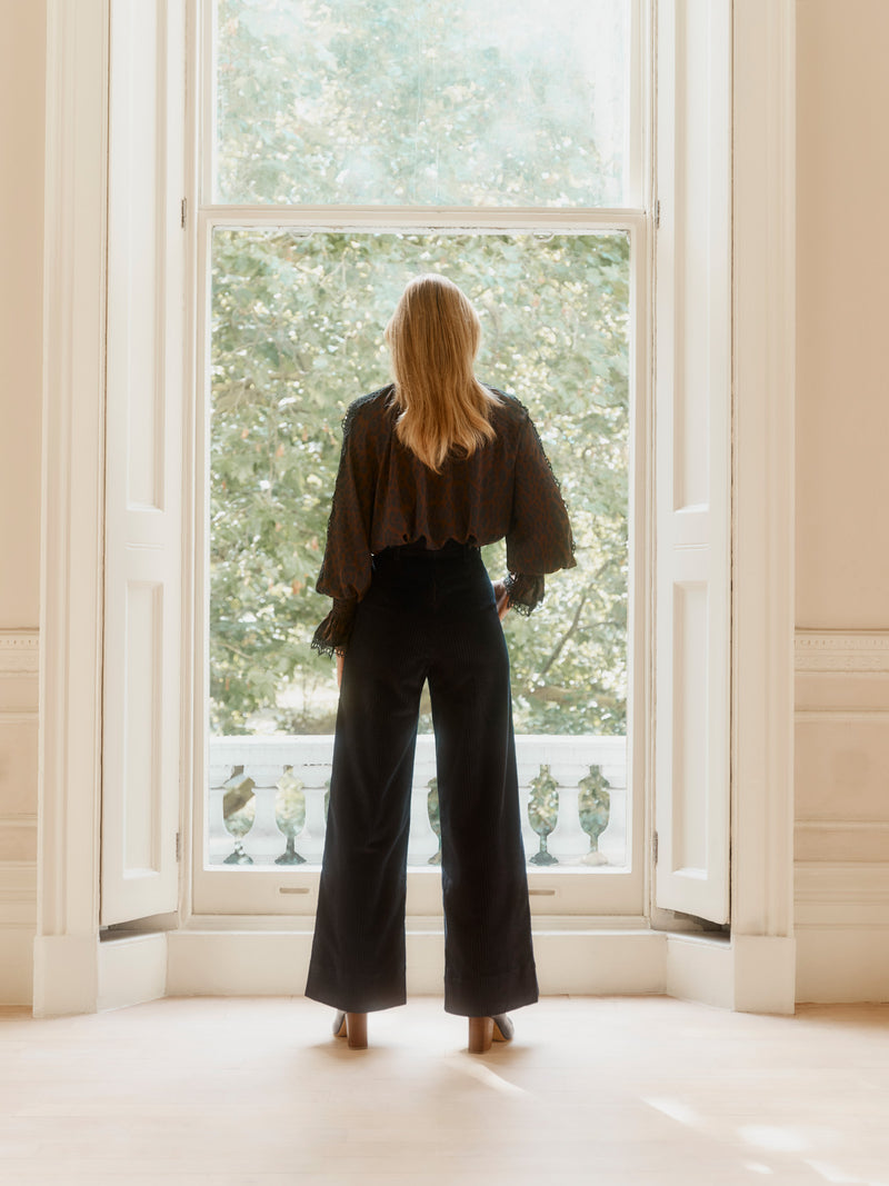 Wiggy Kit model wearing the Pirate Shirt in Leopard and The Sailor Cord trouser facing away and standing in a window, hands on hips.