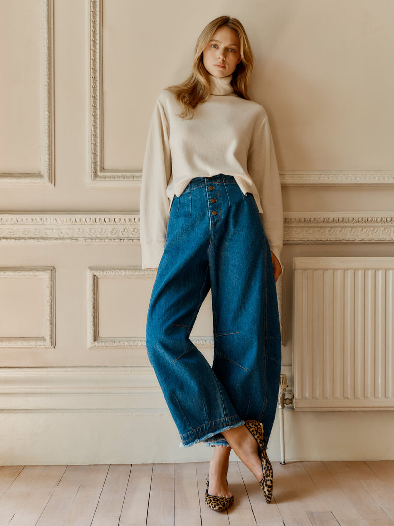 A model wearing the Wiggy Kit Rancher Jean and Inside Out Turtleneck in Ivory leaning on a wall in a grand room.