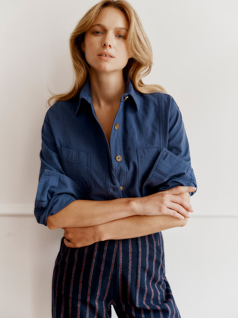 Wiggy Kit model wearing The Yonder Shirt and Ledbury Pant leaning on a wall in a grand house, arms folded.