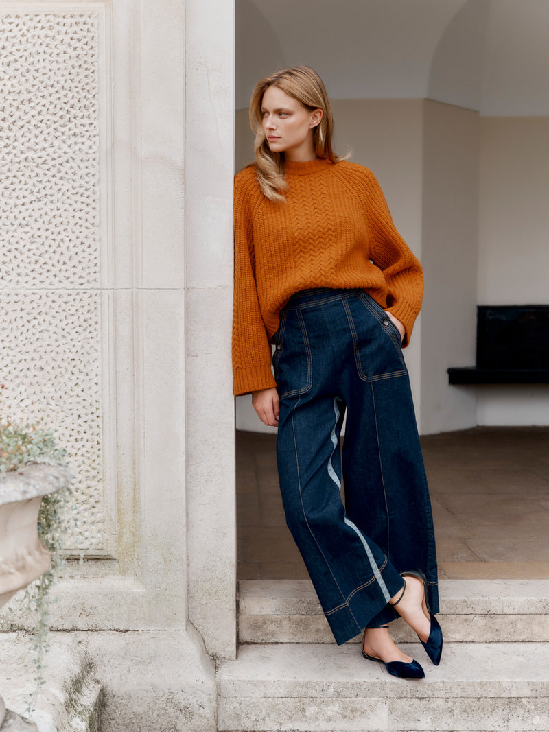 Wiggy Kit model wearing The Inside Stripe Jean and Slouch Fisherman's Crew in orange leaning in a grand doorway.