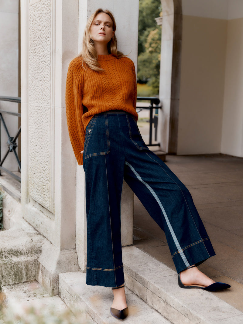 Wiggy Kit model wearing The Inside Stripe Jean and Slouch Fisherman's Crew in orange leaning in a grand doorway, hands behind back.