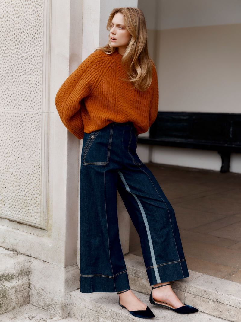 Wiggy Kit model wearing The Inside Stripe Jean and Slouch Fisherman's Crew in orange leaning in a grand doorway, hands behind back.